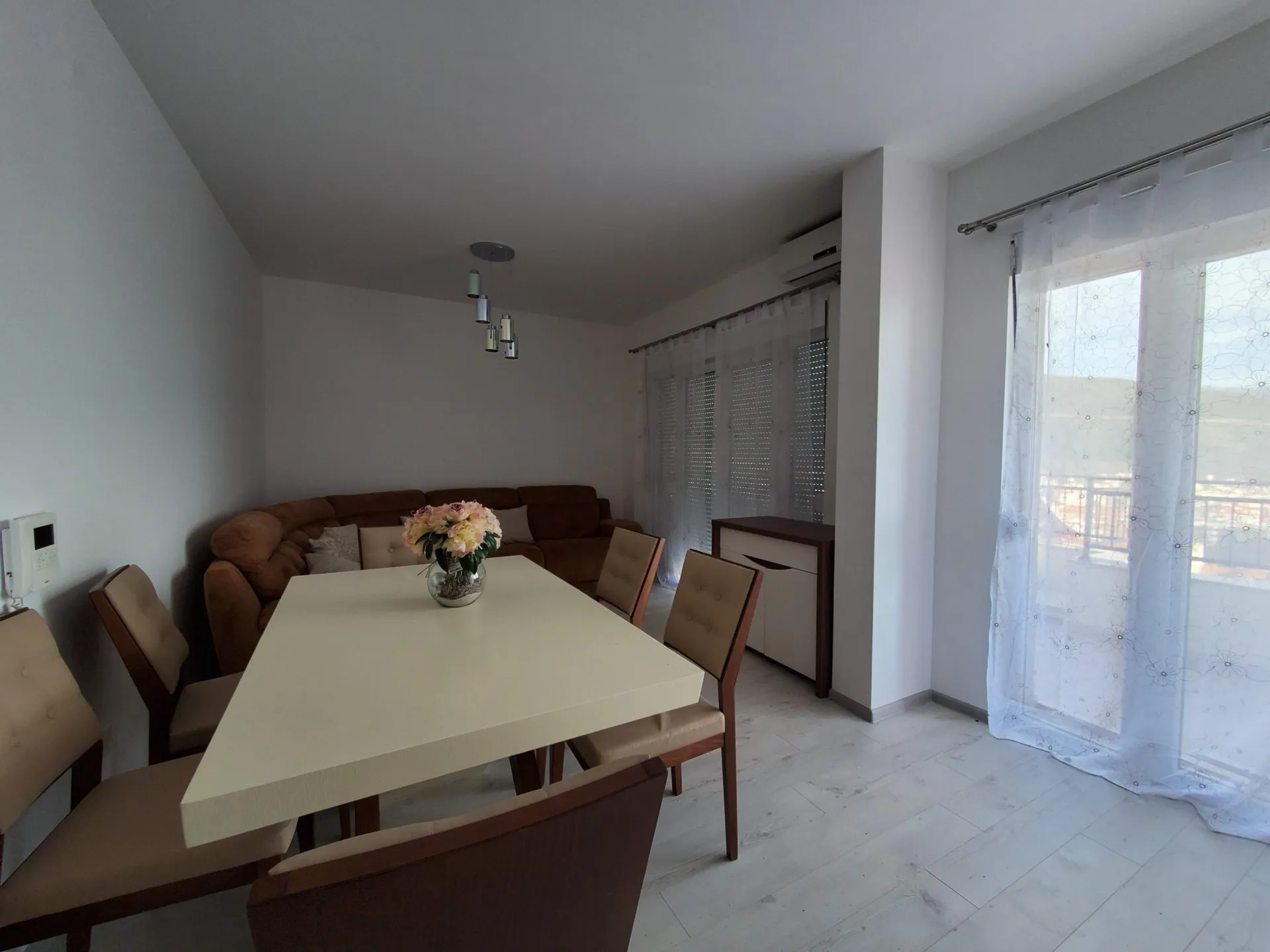 Helles Wohnzimmer mit Essbereich und weichem Sofa in einer Wohnung in Budva, Montenegro. Modernes Interieur mit Zugang zum Balkon.