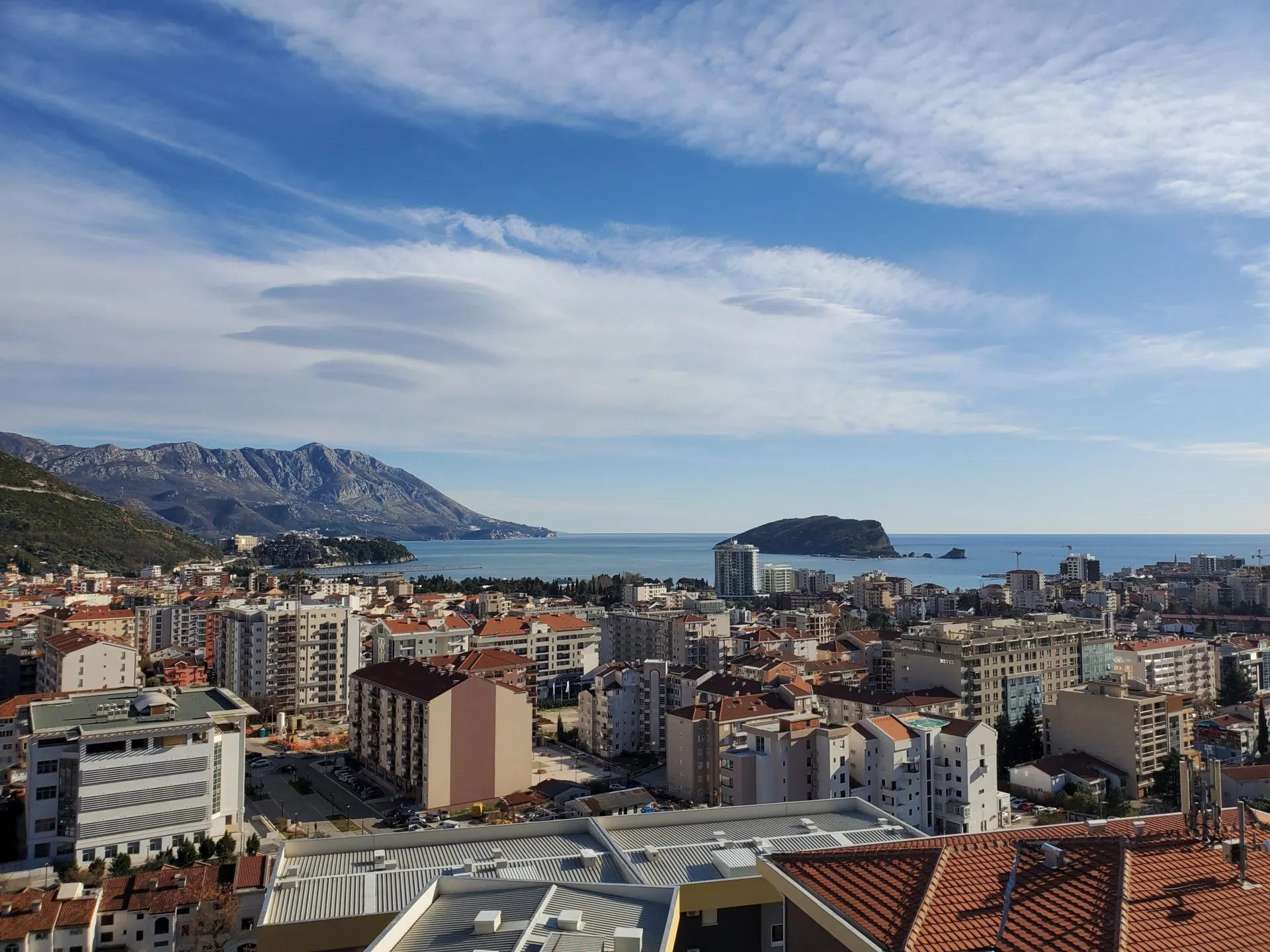 Panoramablick auf die Stadt Budva, das Meer und die Insel Sveti Nikola aus einer Wohnung in Montenegro, Blick aus der Höhe auf die Bebauung.
