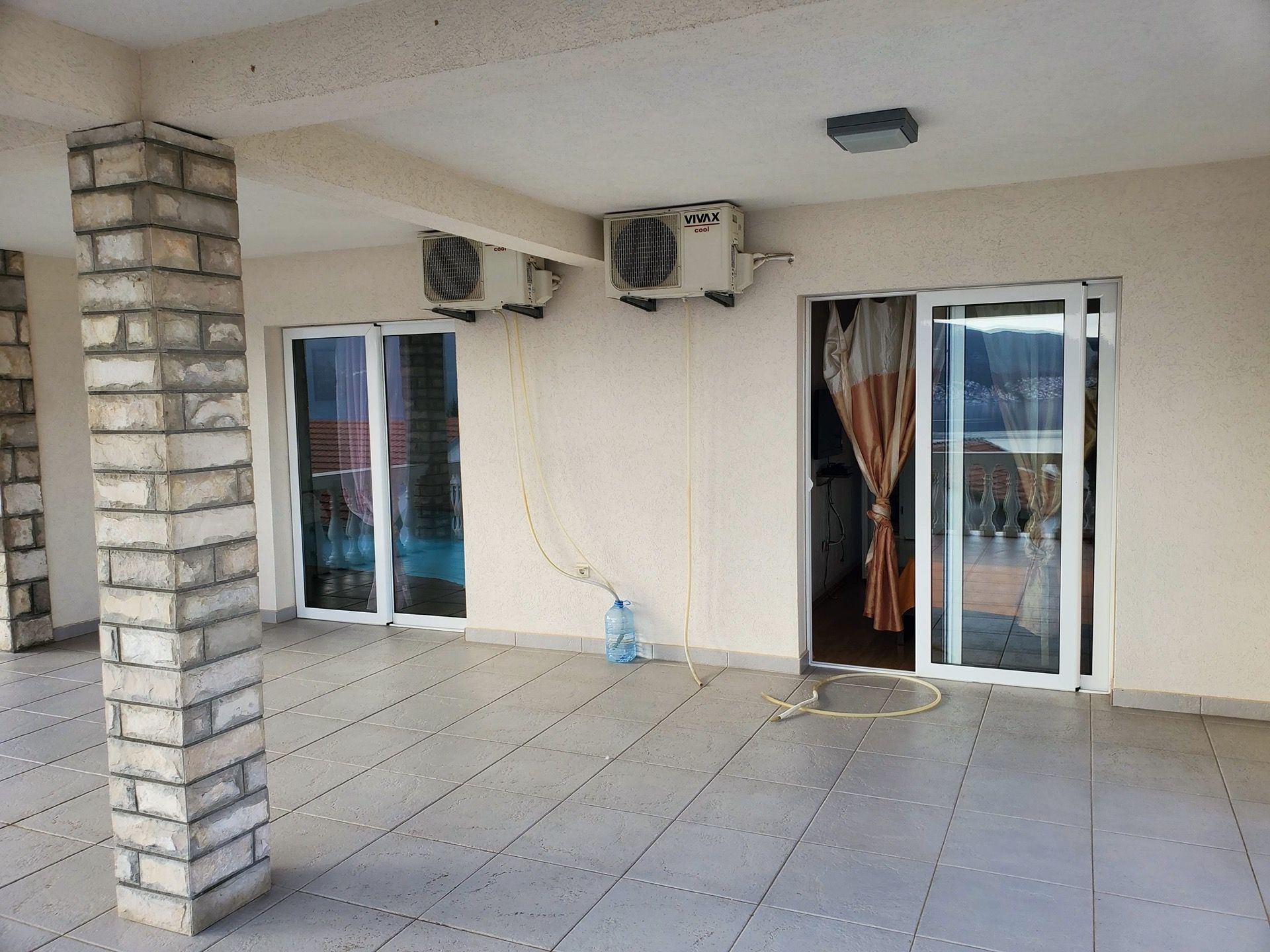 Przestronny taras hotelu w Bijeli, Czarnogóra, z kamienną kolumną, kafelkową podłogą i wyjściem do pokoju przez panoramiczne drzwi.