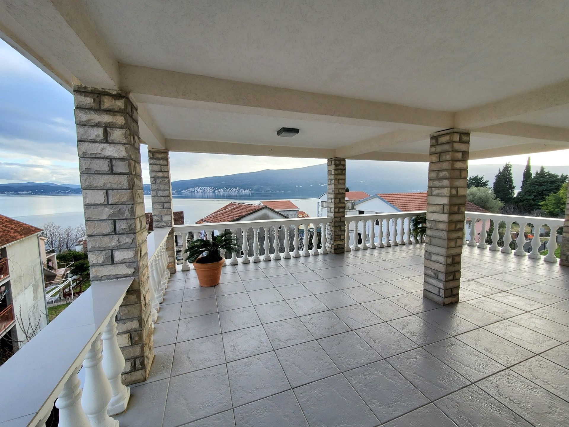 Przestronny taras hotelu w Bijeli, Czarnogóra, z kamiennymi kolumnami, balustradą i panoramicznym widokiem na morze i góry.