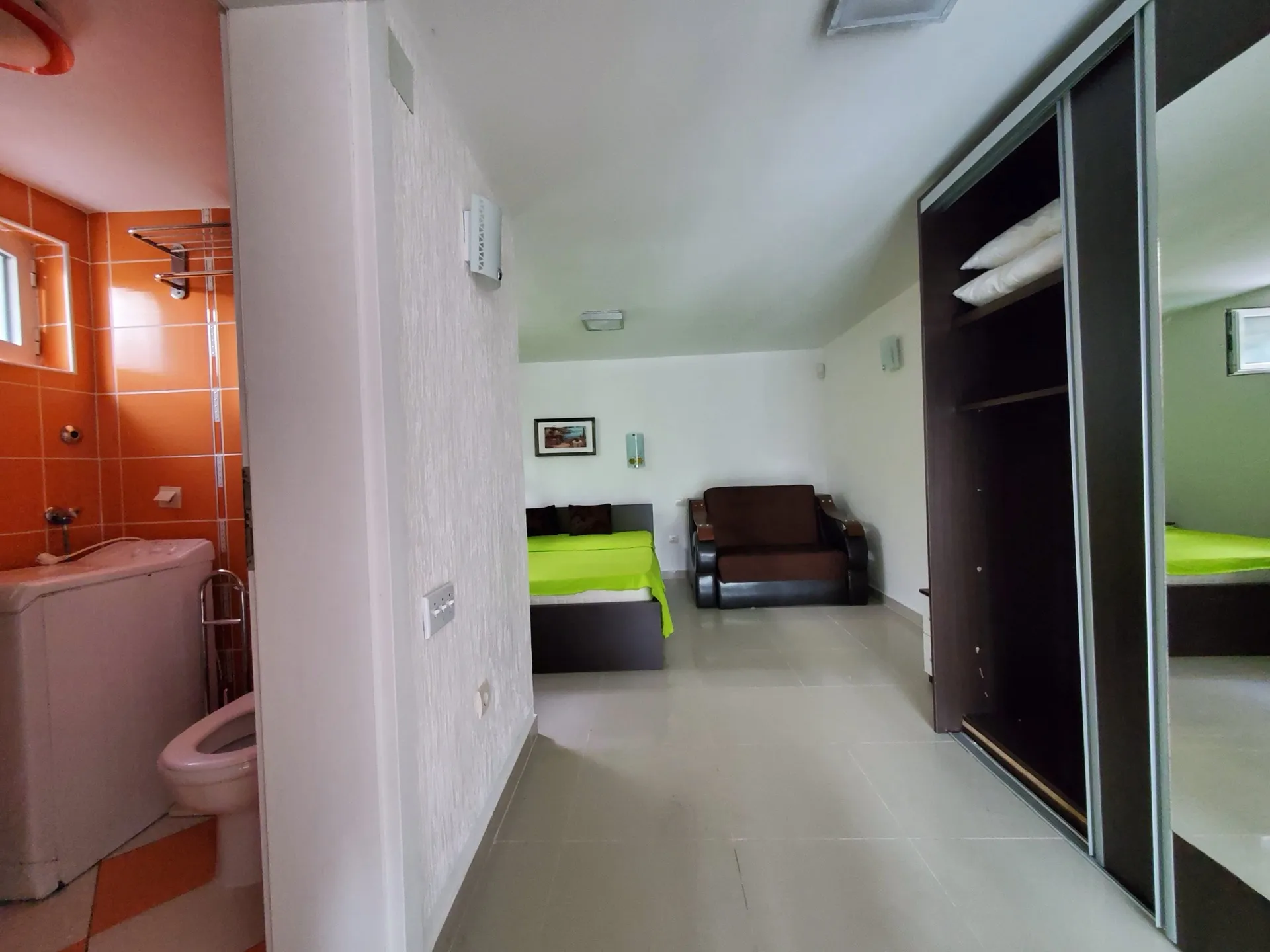 Innenraum eines Hotelzimmers in Bijela, Montenegro: Schlafzimmer mit Bett, Sofa, Kleiderschrank und Badezimmer mit orangefarbenen Fliesen.