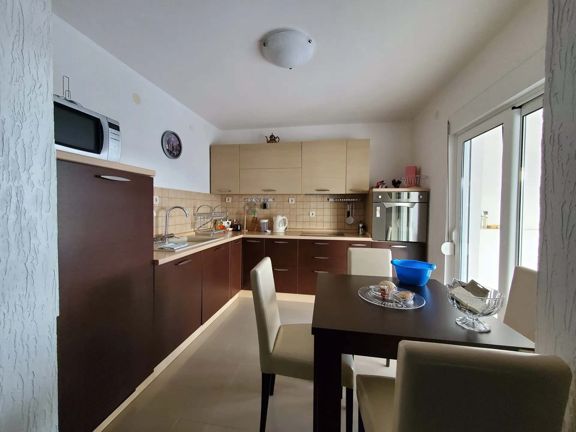Moderne Küche mit Essbereich in einem Hotel in Biele, Montenegro: dunkle Möbel, Einbaugeräte und Zugang zum Balkon.