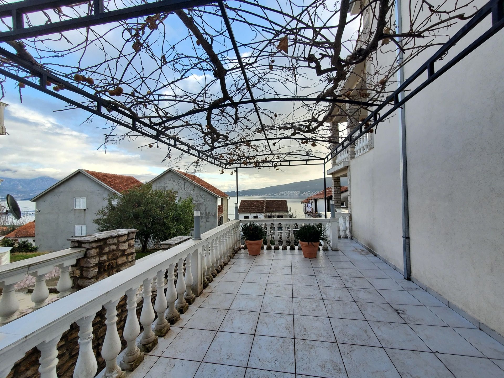 Przestronny taras hotelu w Bijeli, Czarnogóra, z balustradą, zadaszeniem z winorośli i widokiem na morze.