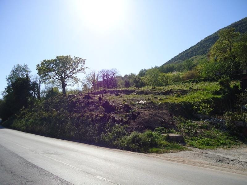 Karadağ, Bijela’da imara uygun arsa: asfalt yol kenarında ağaçlı engebeli arazi.