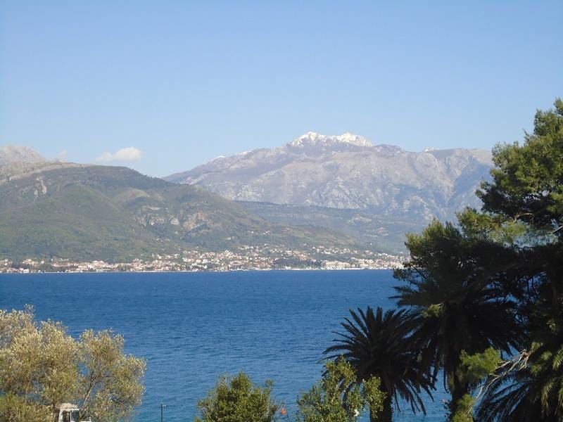 Vue panoramique sur une mer bleue, des collines verdoyantes et des sommets enneigés.