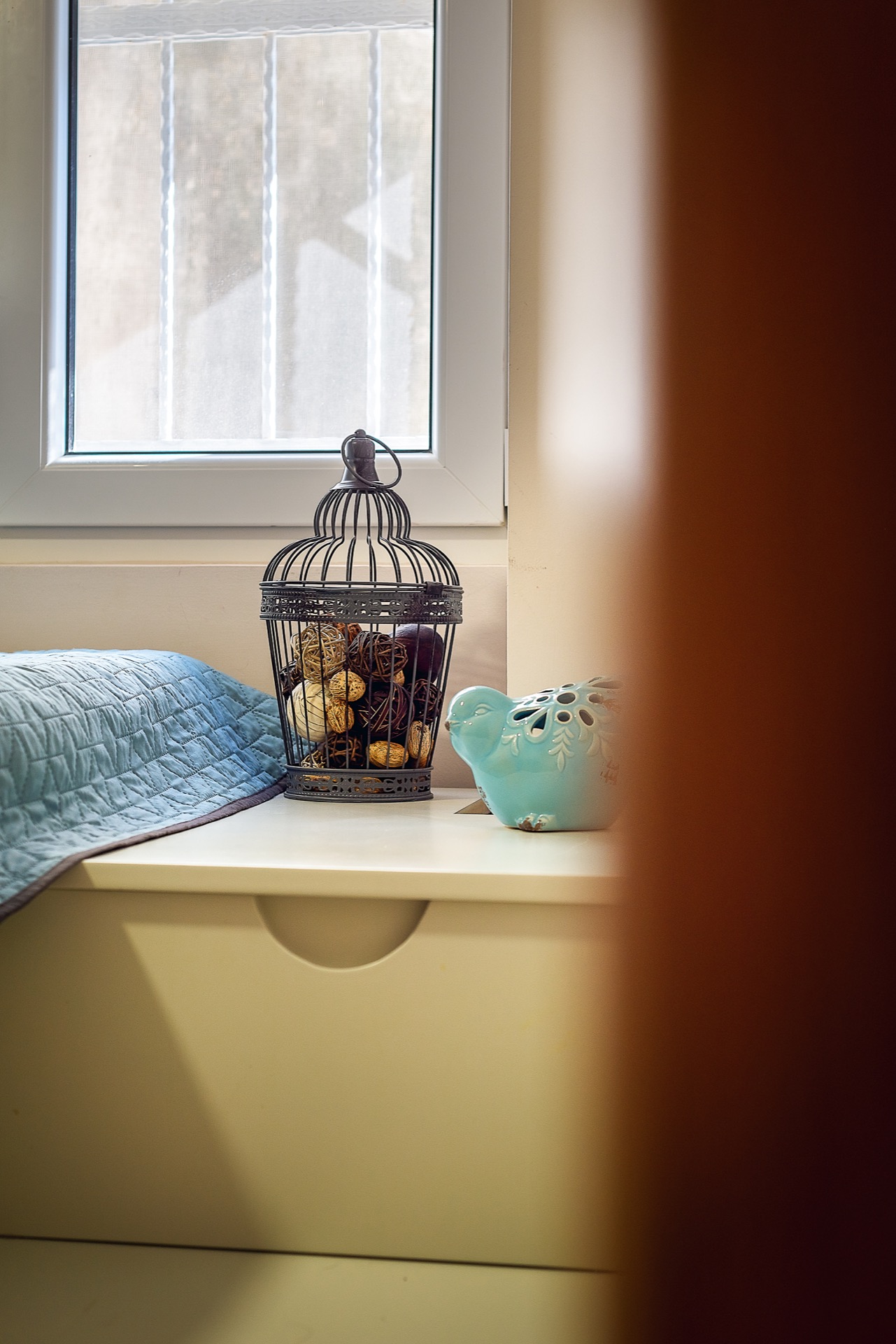Dekor im Schlafzimmer einer Wohnung in Budva, Montenegro: weißer Nachttisch, dekorativer Käfig und Vogelfigur am Fenster.