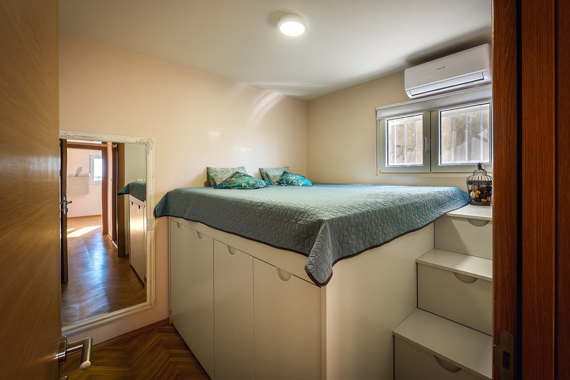 Schlafzimmer in einer Wohnung in Budva, Montenegro: Hochbett mit Stauraum, Treppe, Spiegel und Klimaanlage.