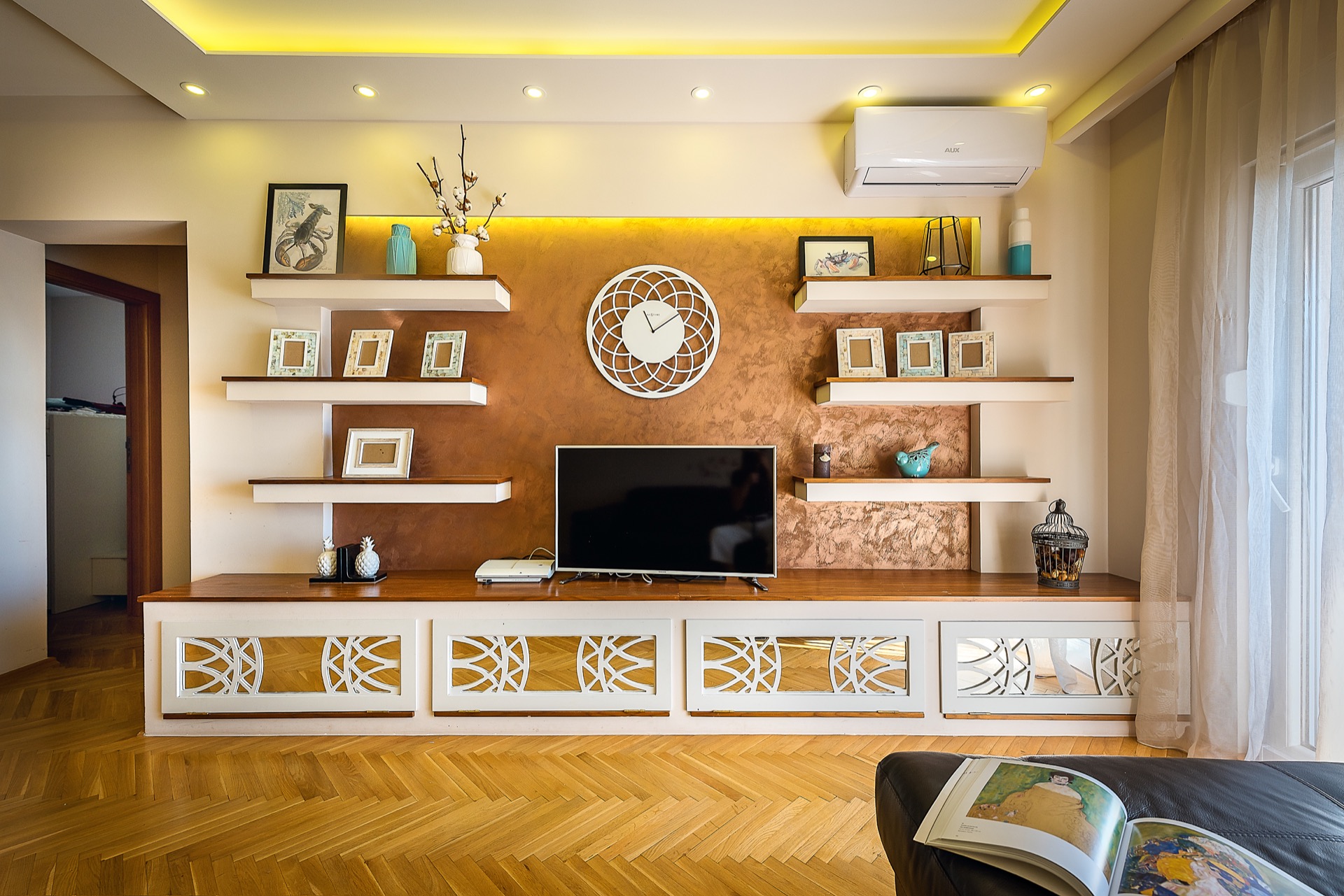 Modernes Wohnzimmer in einer Wohnung in Budva, Montenegro: TV-Bereich mit dekorativen Regalen, Beleuchtung und Parkettboden.