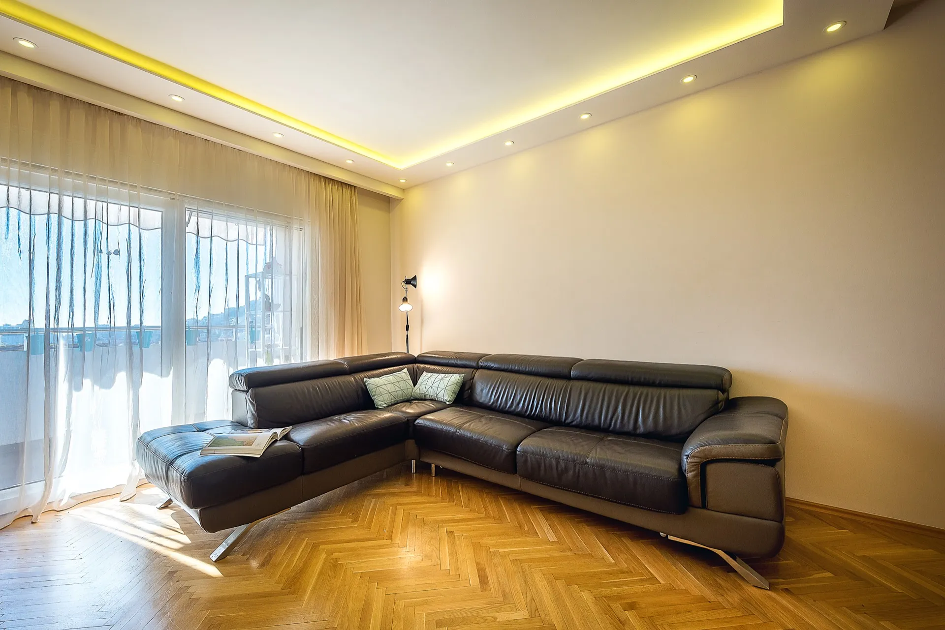 Modern living room with a leather corner sofa and parquet flooring in an apartment in Budva, Montenegro, with access to the balcony.