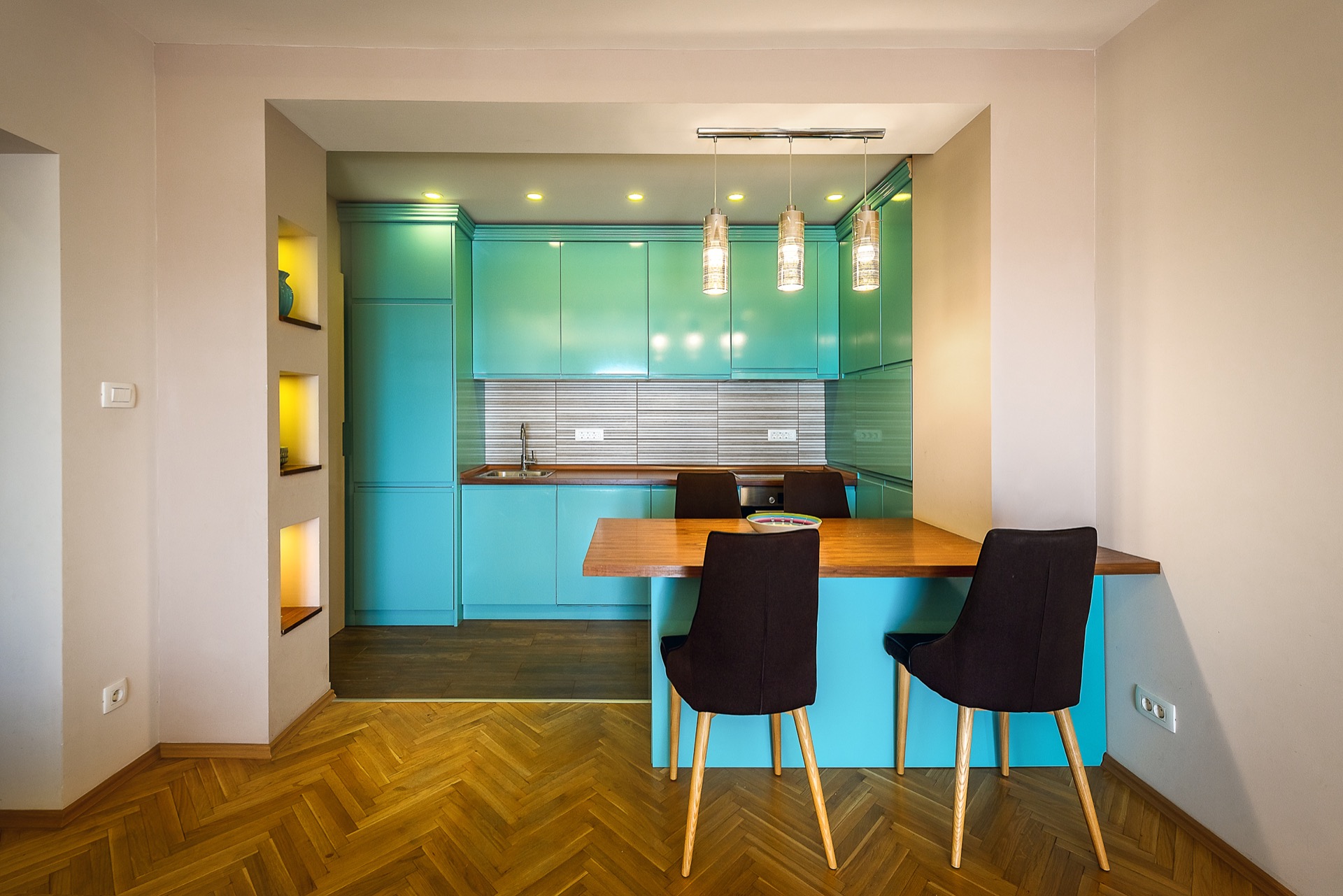 Moderne Küche mit türkisfarbener Einbauküche und Essbereich in einer Wohnung in Budva, Montenegro. Parkettboden, Beleuchtung.