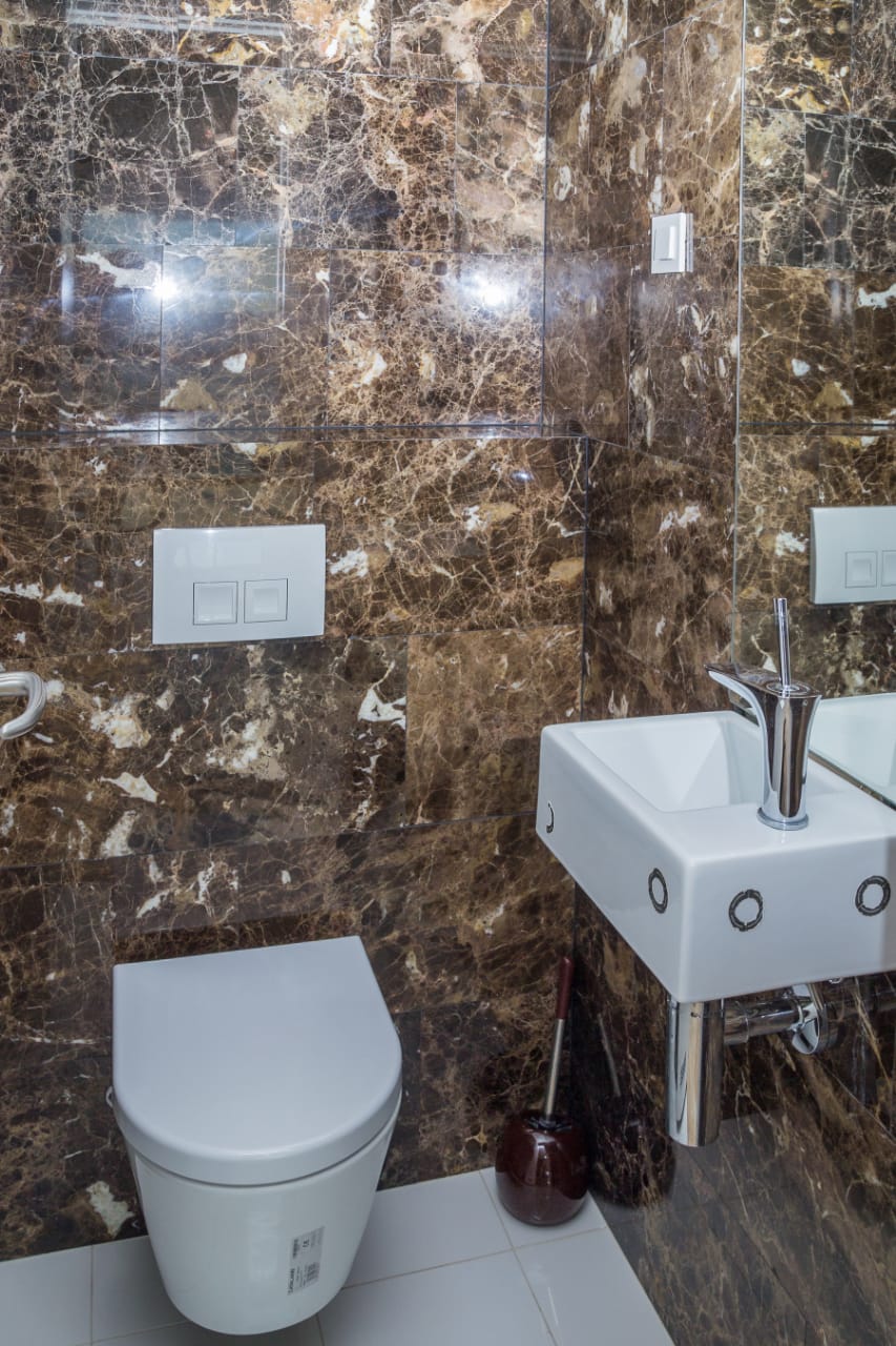 Badezimmer in einer Wohnung in Budva, Montenegro: Wände mit braunem Marmor verkleidet, wandhängendes WC und weißes Waschbecken.