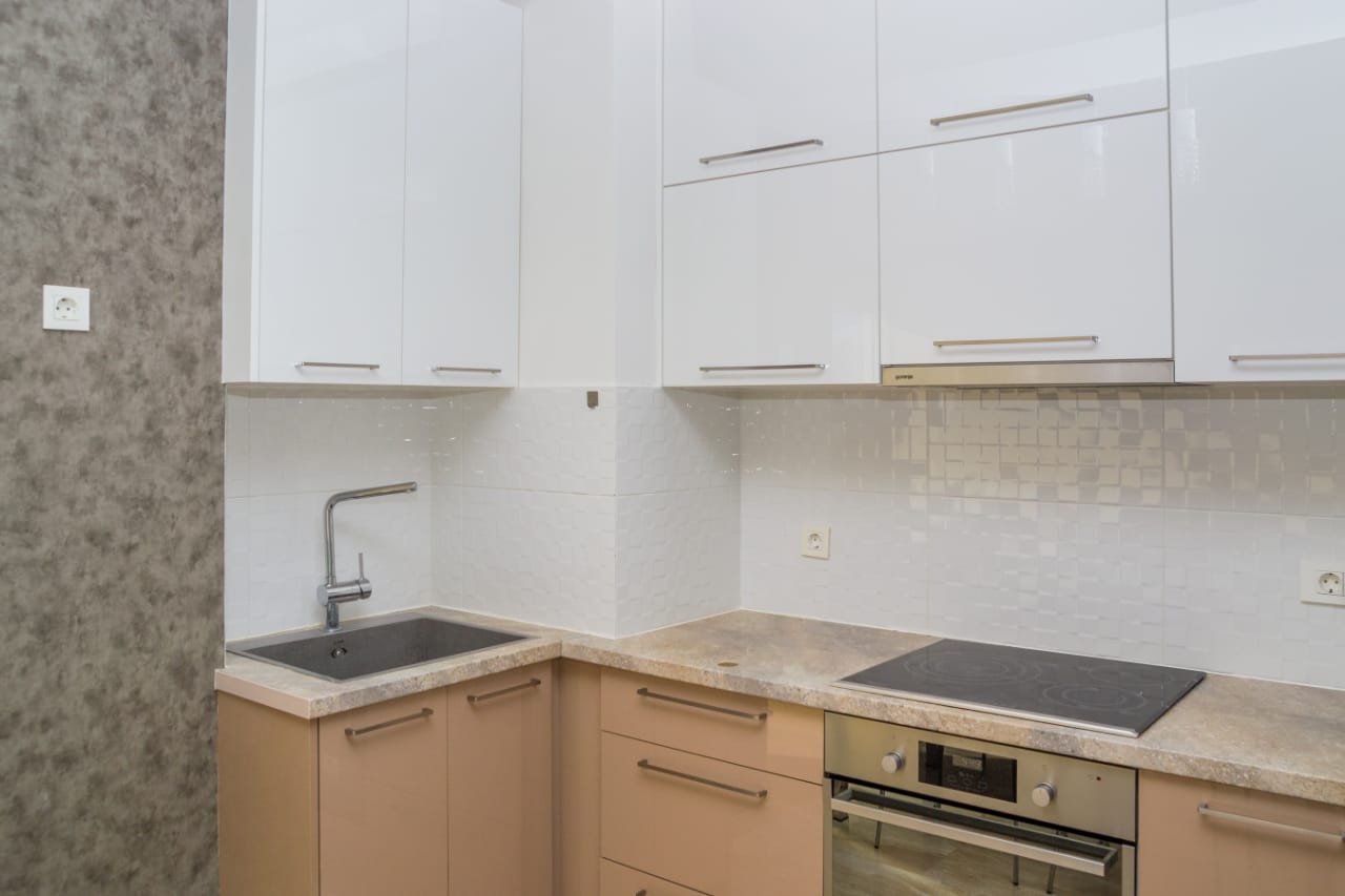 Moderne Küche in einer Wohnung in Budva, Montenegro: weiße Hochglanzschränke, Einbaugeräte und eine Steinarbeitsplatte.