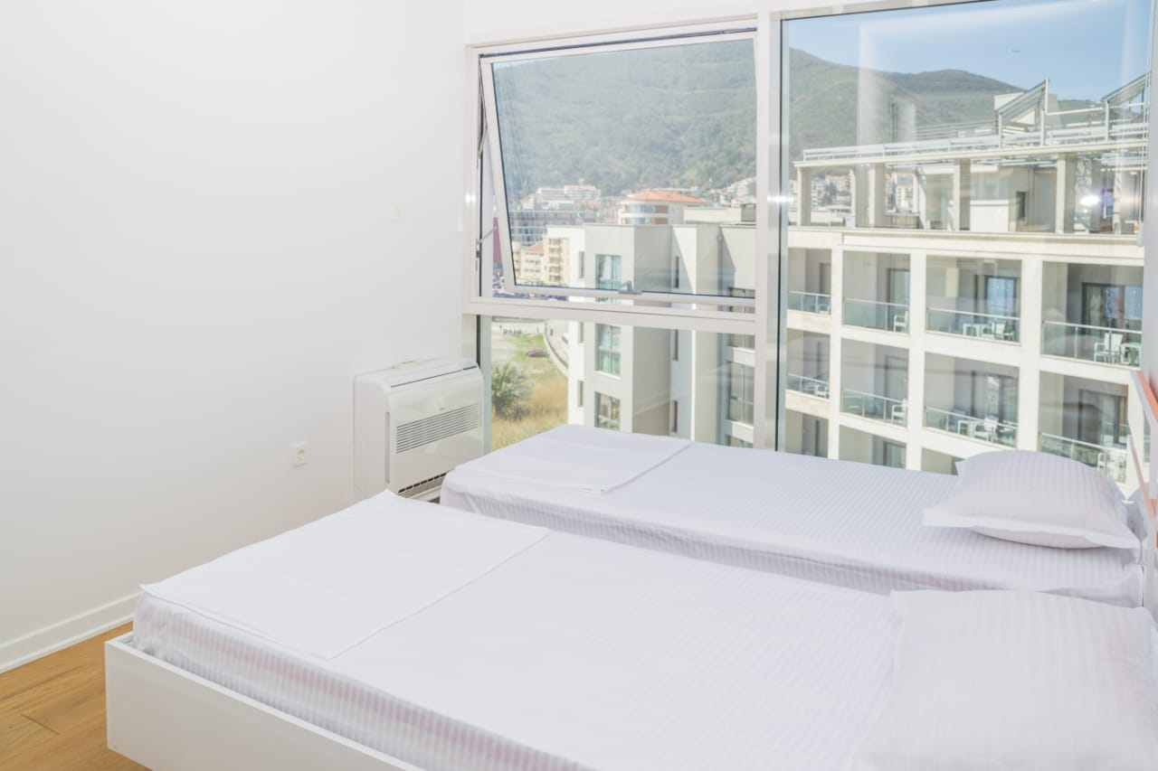 Helles Schlafzimmer mit zwei Betten und Panoramablick auf die Berge in einer Wohnung in Budva, Montenegro.