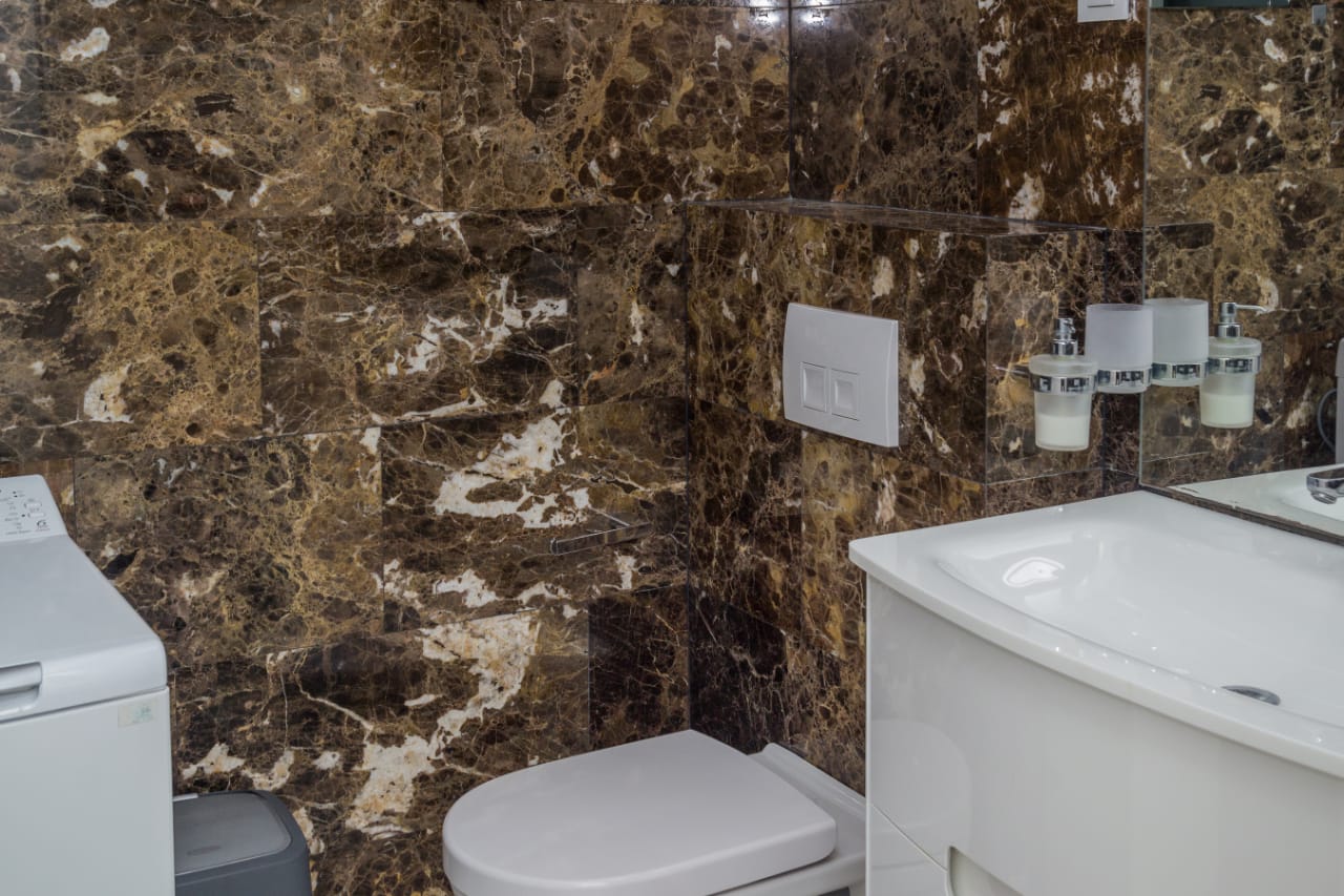 Badezimmer in einer Wohnung in Budva, Montenegro: Wände mit braunem Marmor verkleidet, weiße Sanitärkeramik und Waschmaschine.