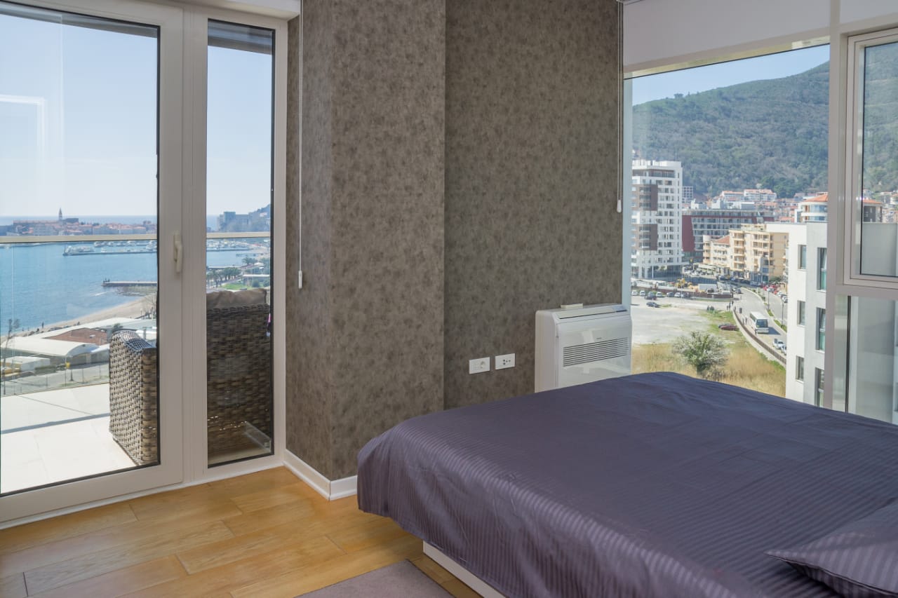 Schlafzimmer in einer Wohnung in Budva, Montenegro: Panoramafenster mit Meerblick, Doppelbett und modernes Interieur.