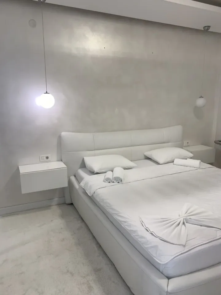 Ein modernes weißes Schlafzimmer mit Doppelbett, Nachttischen und Hängeleuchten.