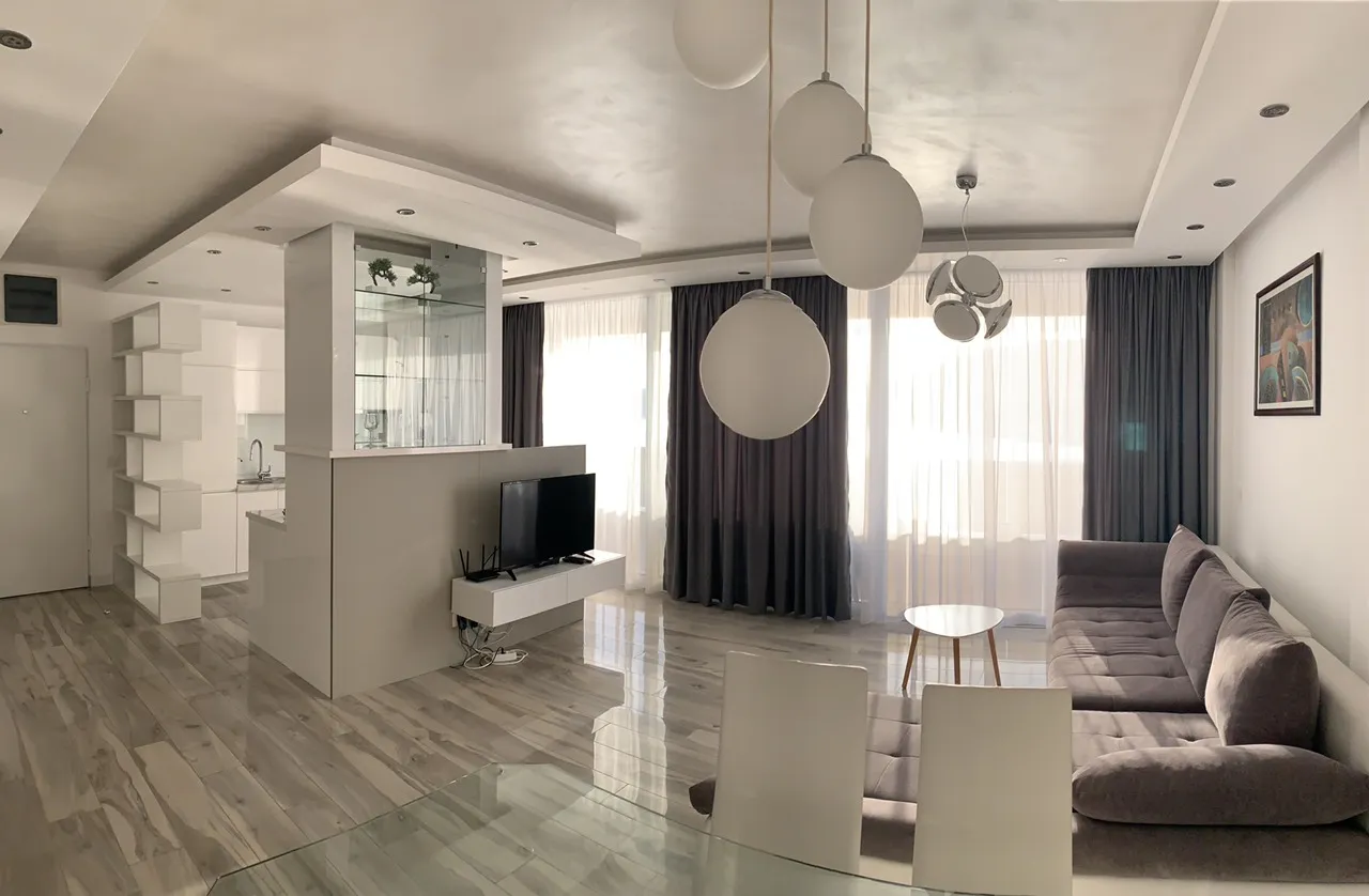 Geräumiges Wohnzimmer mit Sofa, Küchenbereich und großen Fenstern.