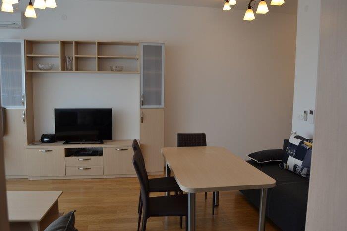 Living room with dining area and light-colored furniture in an apartment in Bečići, Montenegro. Modern interior with a TV wall unit.