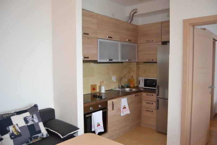 Modern kitchen in an apartment in Bečići, Montenegro: wooden fronts, built-in appliances, and a dining area with a sofa.
