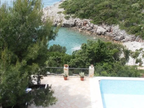 Eine Außenterrasse mit einem Swimmingpool und Blick auf eine Meeresbucht und grüne Landschaft.