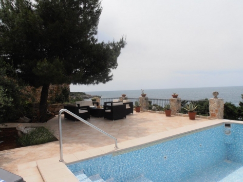 Terrasse mit Pool und Meerblick an einer Villa in Luštica, Montenegro: geflochtene Sessel, Steinverkleidung und Landschaftsgestaltung.