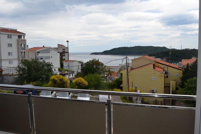 View from the apartment balcony in Bečići, Montenegro: a panorama of the sea, mountains, and residential buildings with modern facade finishes.