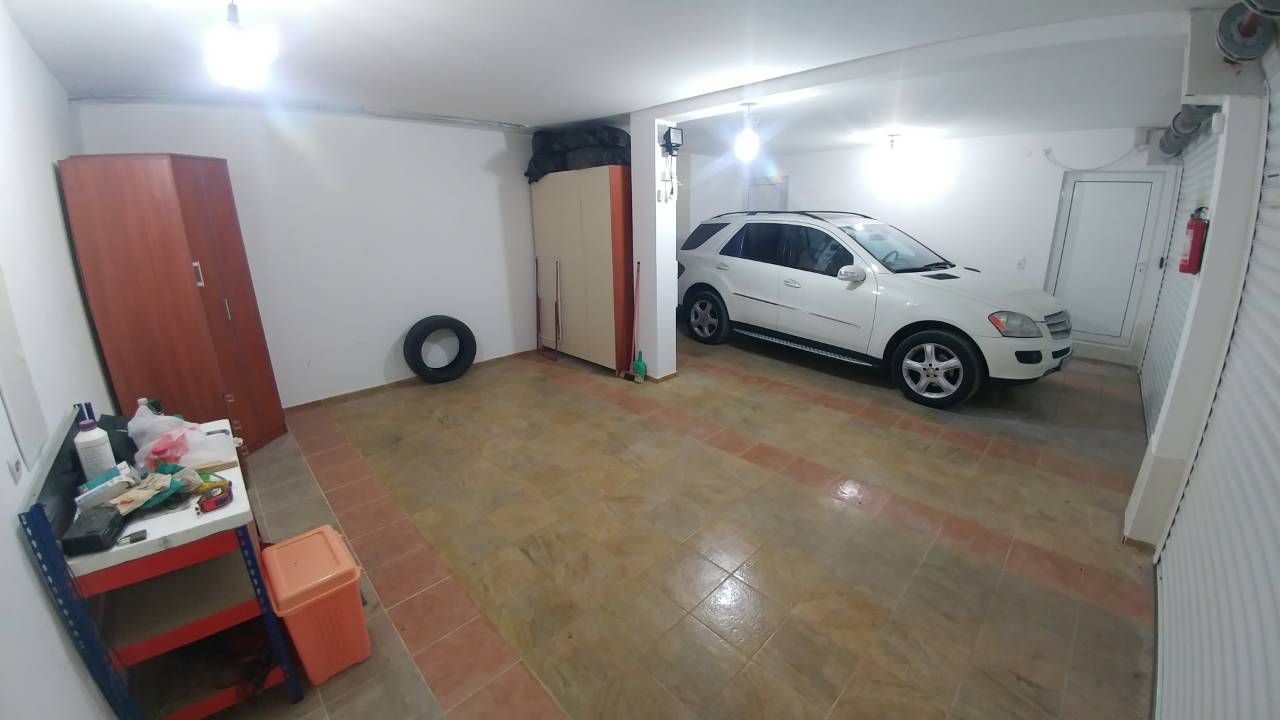 Un garage spacieux avec une voiture blanche, un meuble de rangement, un établi et un pneu sur le mur.