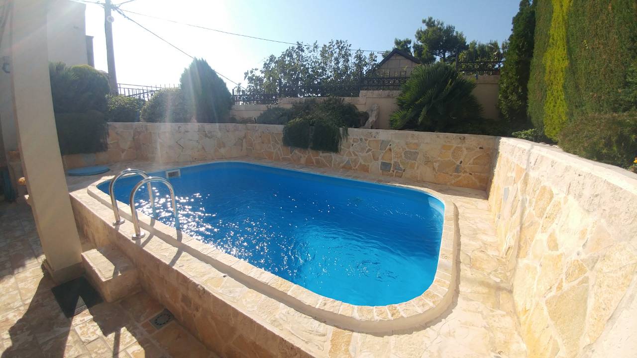 Piscine extérieure entourée d'un mur en pierre et de verdure dans un jardin.