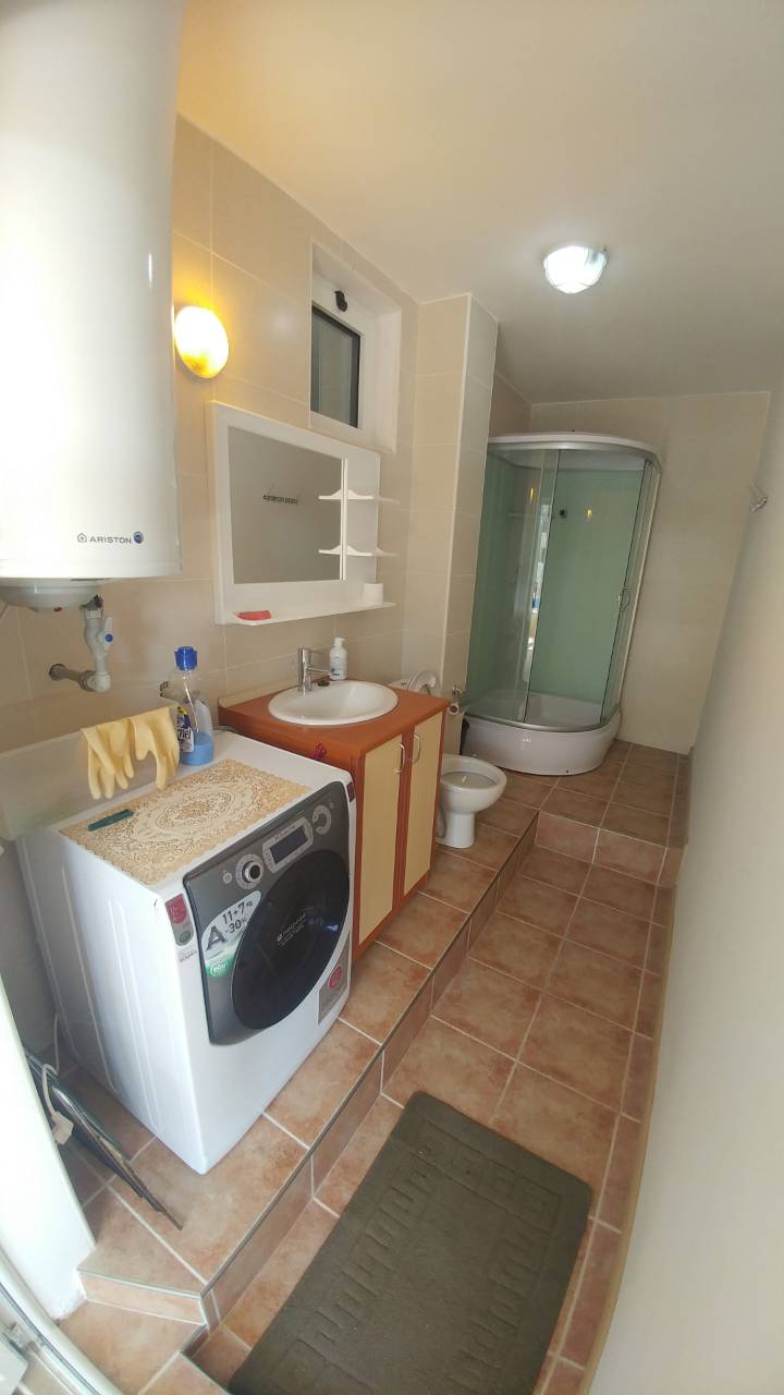 Une salle de bain compacte avec cabine de douche, lavabo, toilettes, machine à laver et chauffe-eau au mur.