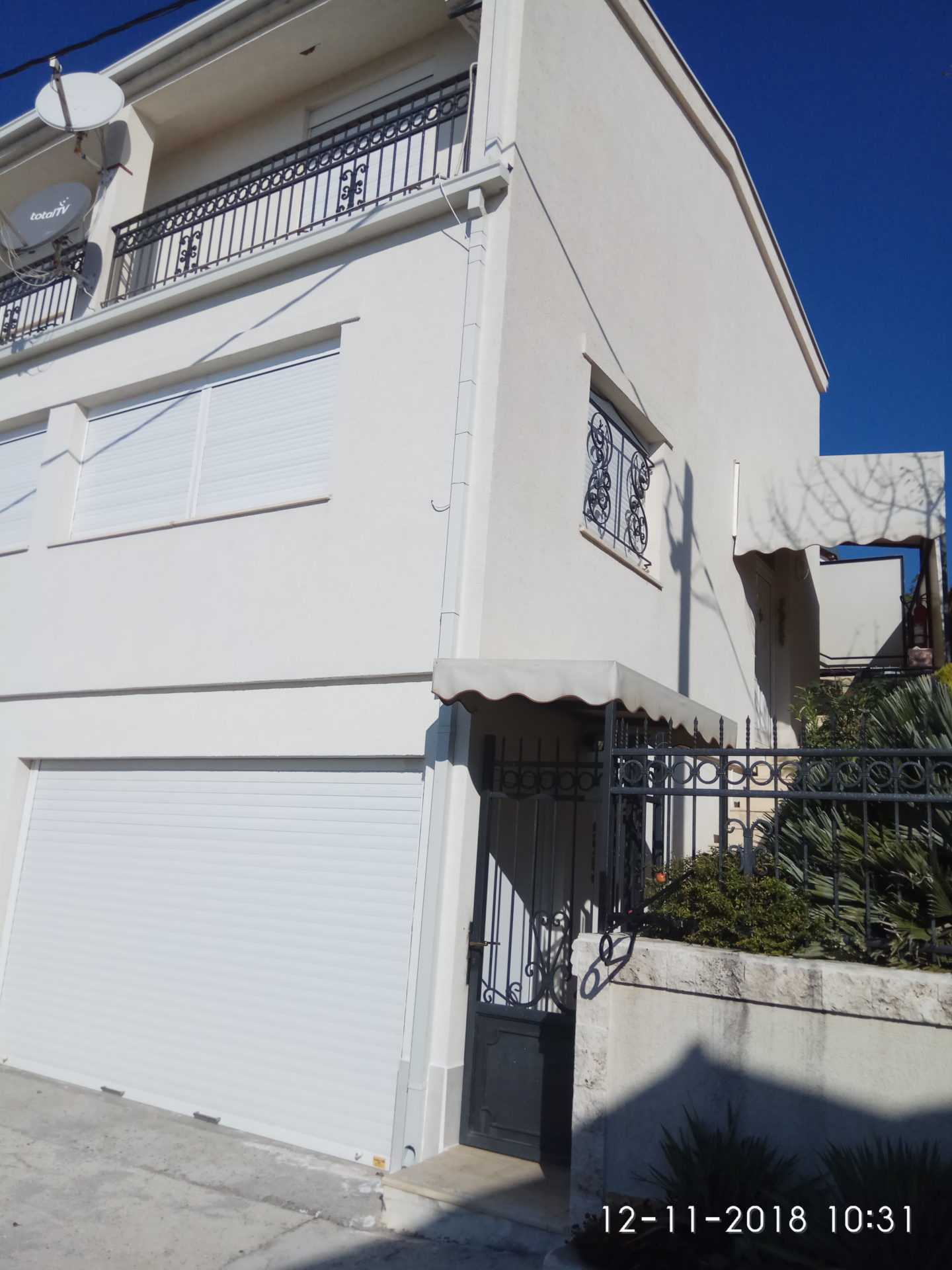 Extérieur d'un bâtiment blanc à deux étages avec garage, balcon et portail.