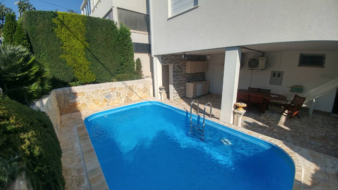 Piscine extérieure dans la cour d'une maison avec mobilier de terrasse et verdure.