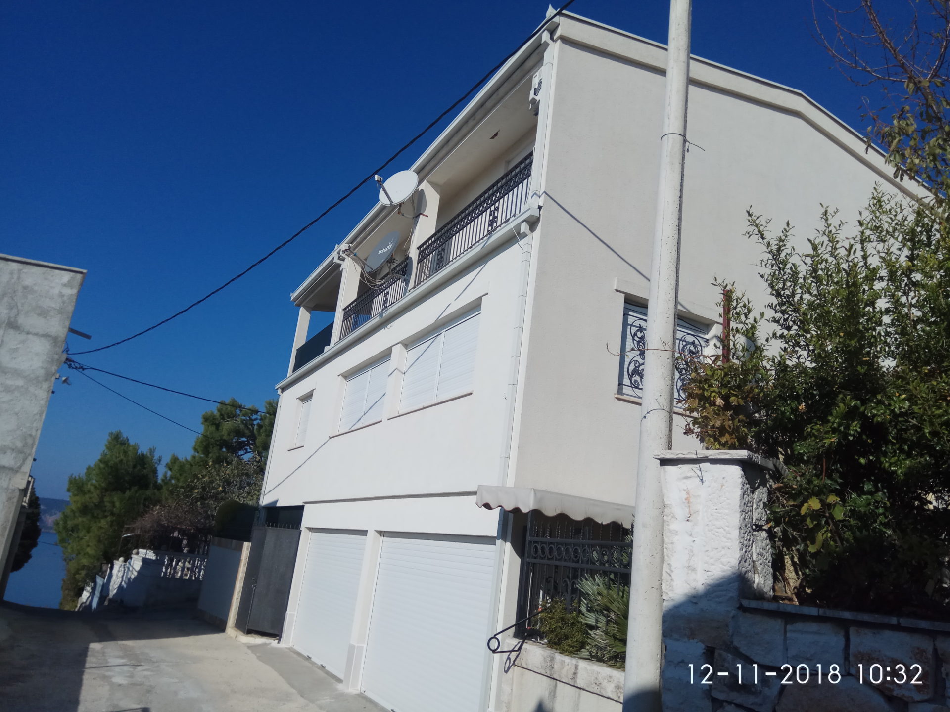 Vue en contre-plongée d'une maison blanche de trois étages avec garages et balcon sous un ciel clair.