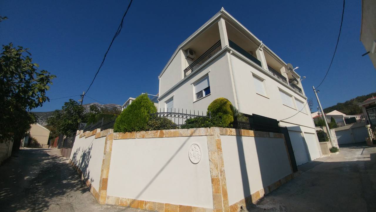 Une maison moderne à deux étages avec un mur d'enceinte en pierre et une ruelle pavée.