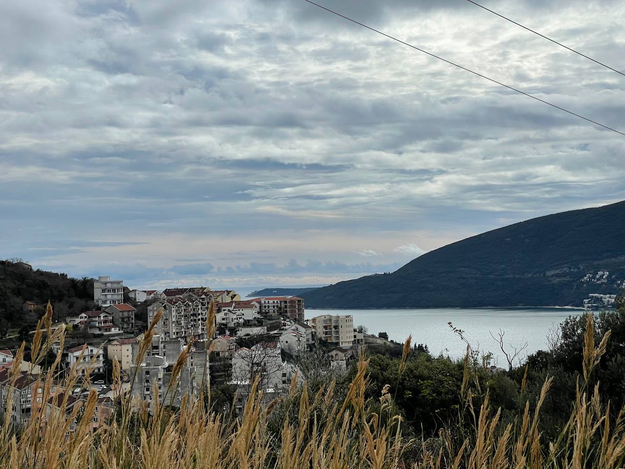 Blick auf Gebäude am Meer, umgeben von Hügeln und bewölktem Himmel.