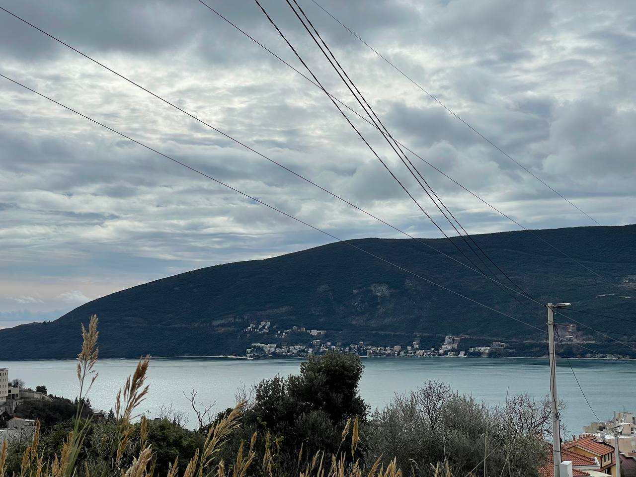 Blick auf das Meer, die Berge und den bewölkten Himmel aus der Höhe mit Stromleitungen im Vordergrund