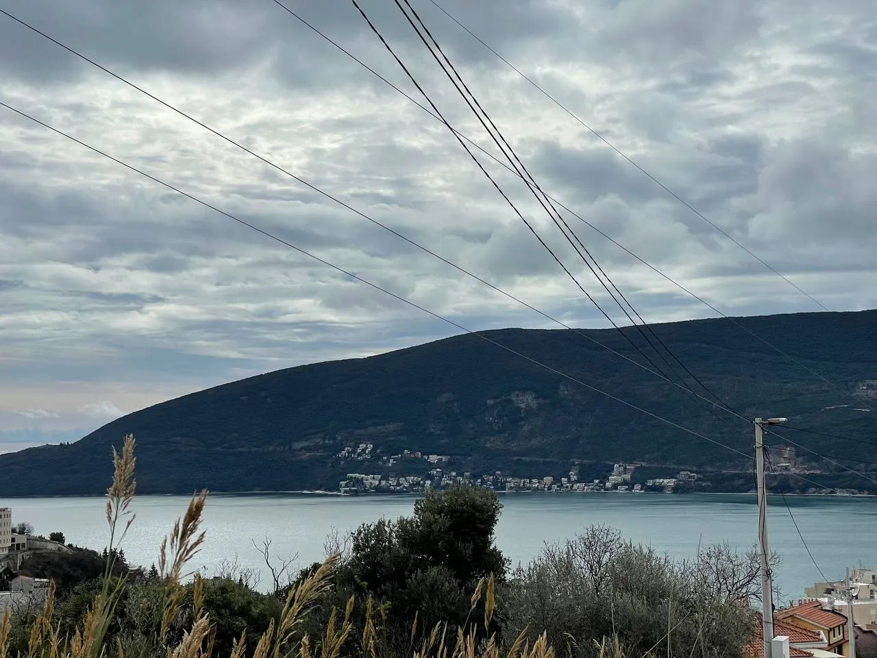 Blick auf das Meer, die Berge und den bewölkten Himmel aus der Höhe mit Stromleitungen im Vordergrund