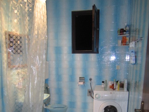 Badezimmer in einem Haus in Tivat, Montenegro: blaue Fliesen, Duschkabine mit Vorhang und Waschmaschine.