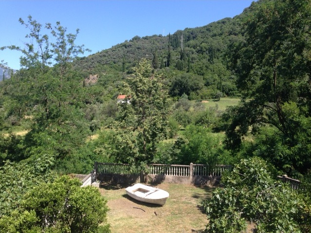 Blick auf einen grünen Garten mit Boot und Berge am Haus in Tivat, Montenegro. Grundstück mit Balustrade und dichter Vegetation.