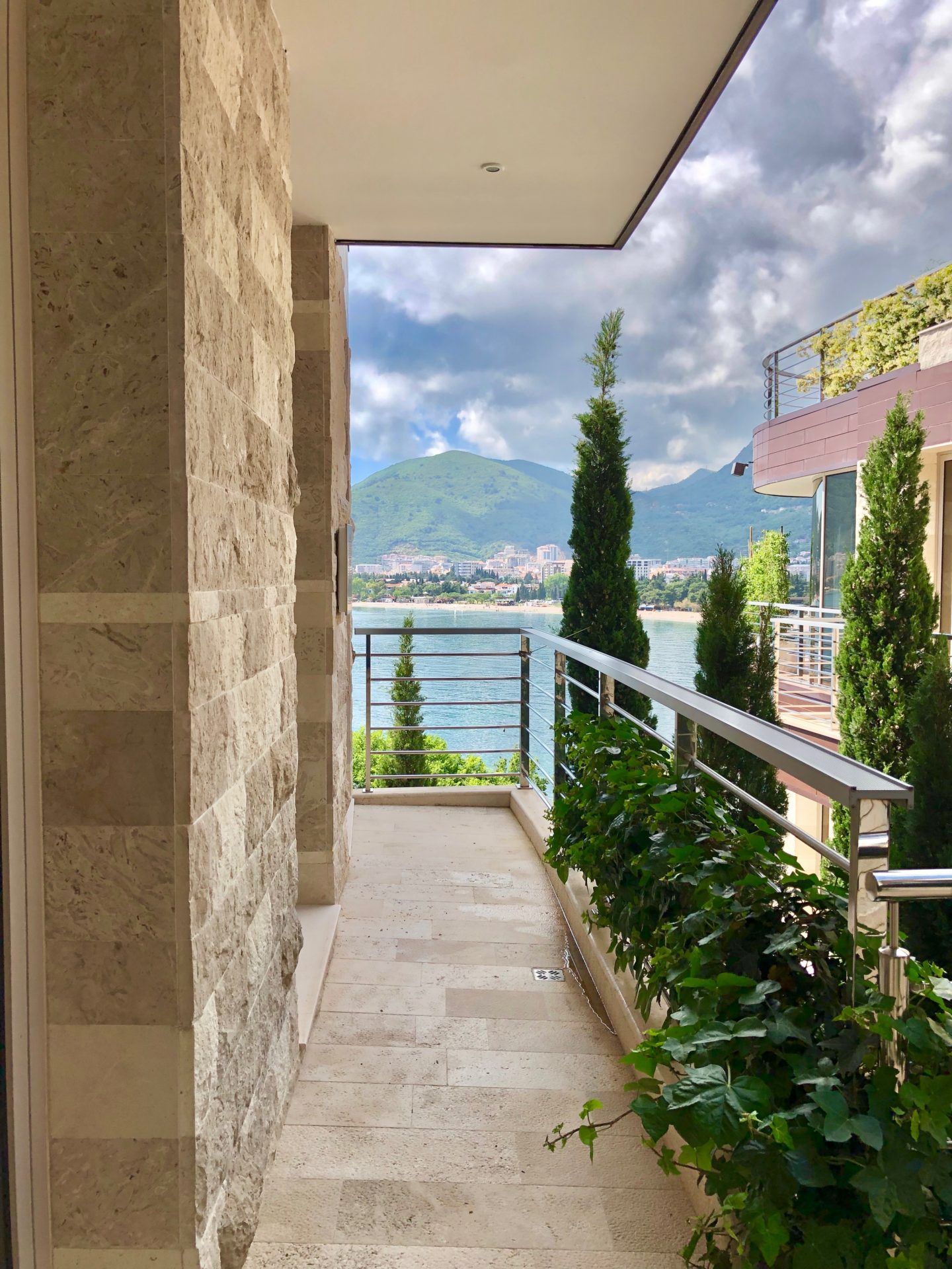 Balkon einer Wohnung in Budva, Montenegro: Steinverkleidung, Meer- und Bergblick, Begrünung und modernes Geländer.