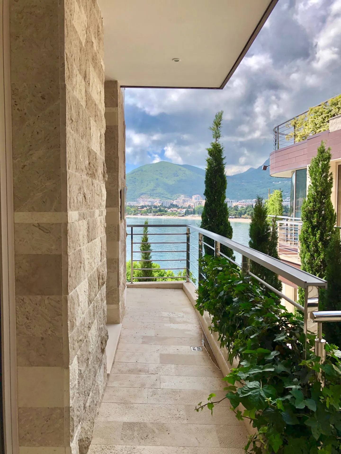 Balkon einer Wohnung in Budva, Montenegro: Steinverkleidung, Meer- und Bergblick, Begrünung und modernes Geländer.