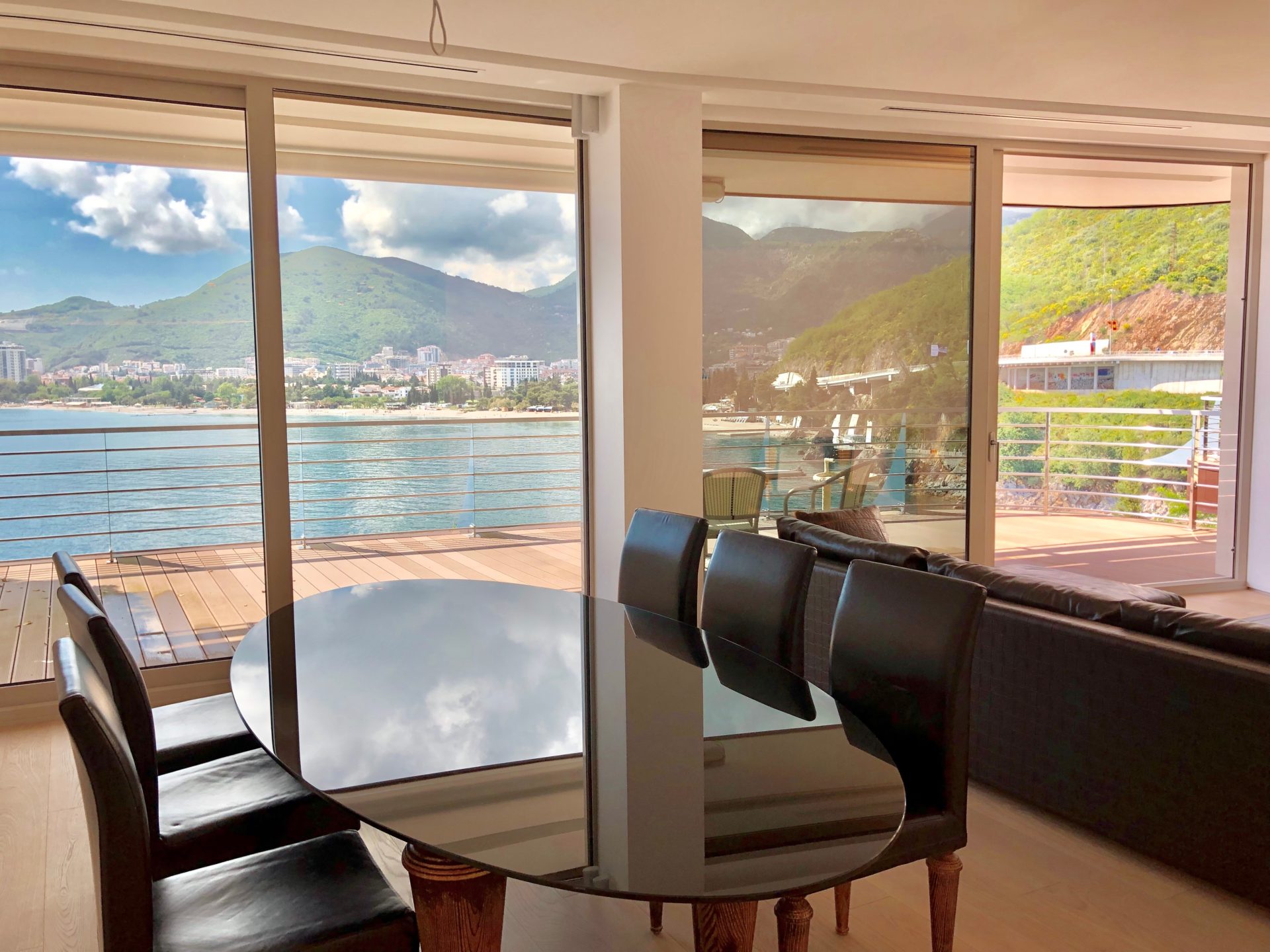 Wohnzimmer mit Panoramablick auf das Meer und die Berge in einer Wohnung in Budva, Montenegro: Esstisch und Terrasse.