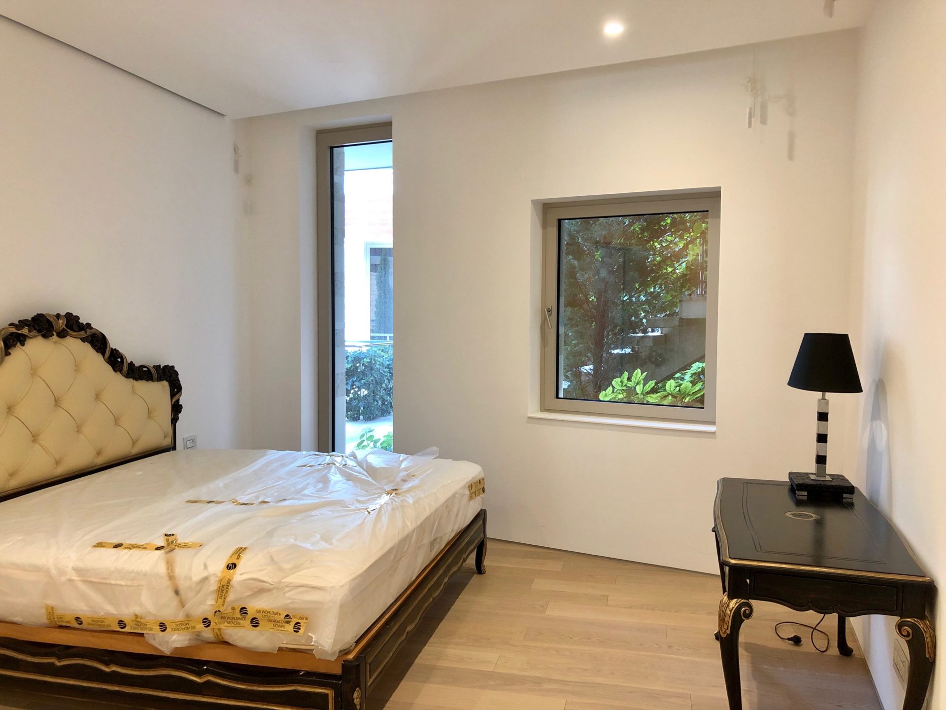Schlafzimmer in einer Wohnung in Budva, Montenegro: klassisches Bett, schwarzer Schminktisch, heller Boden und Blick auf den Garten.