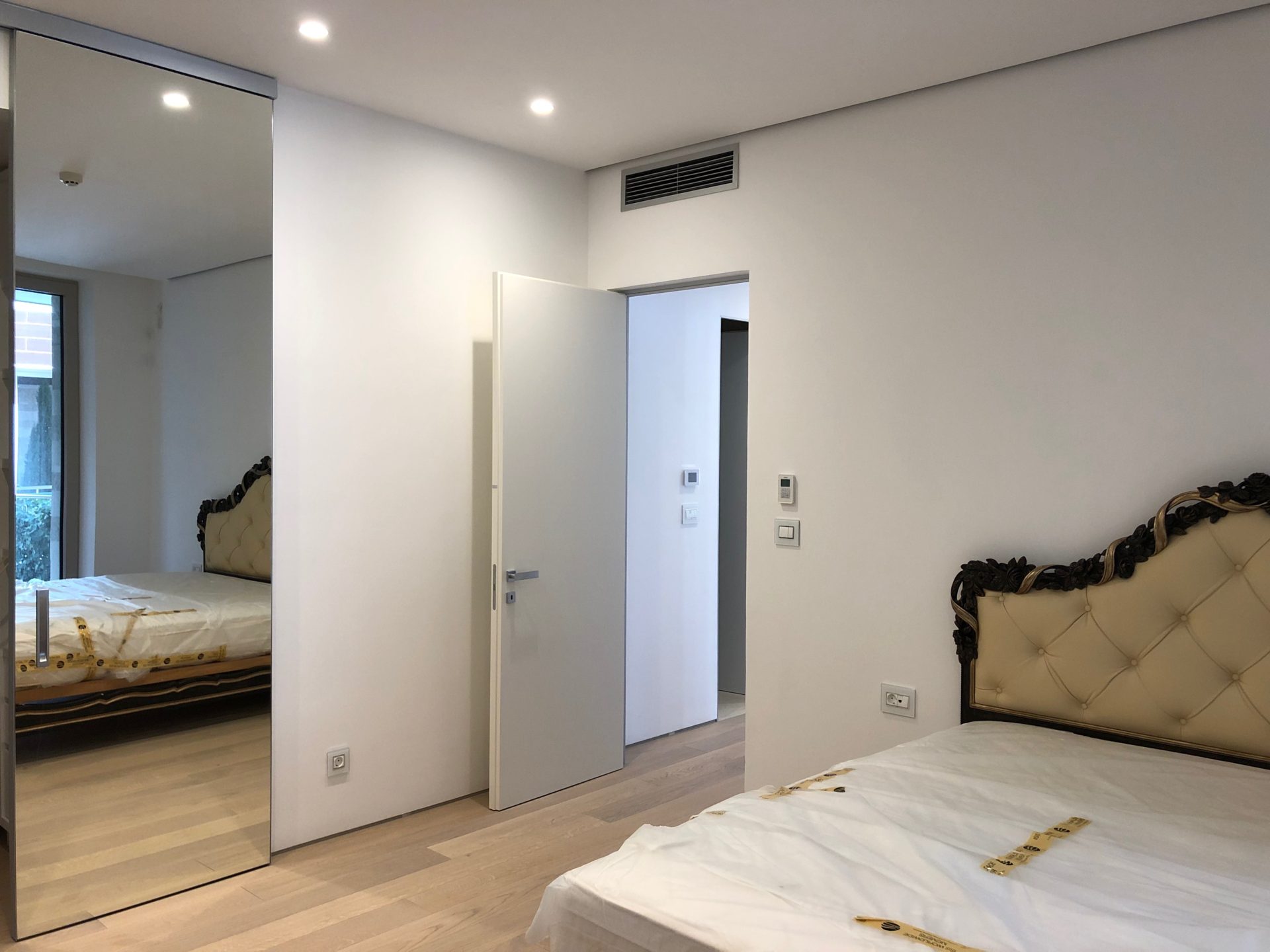 Modernes Schlafzimmer in einer Wohnung in Budva, Montenegro: Bett mit klassischem Kopfteil, Kleiderschrank mit Spiegeltüren und Parkett.