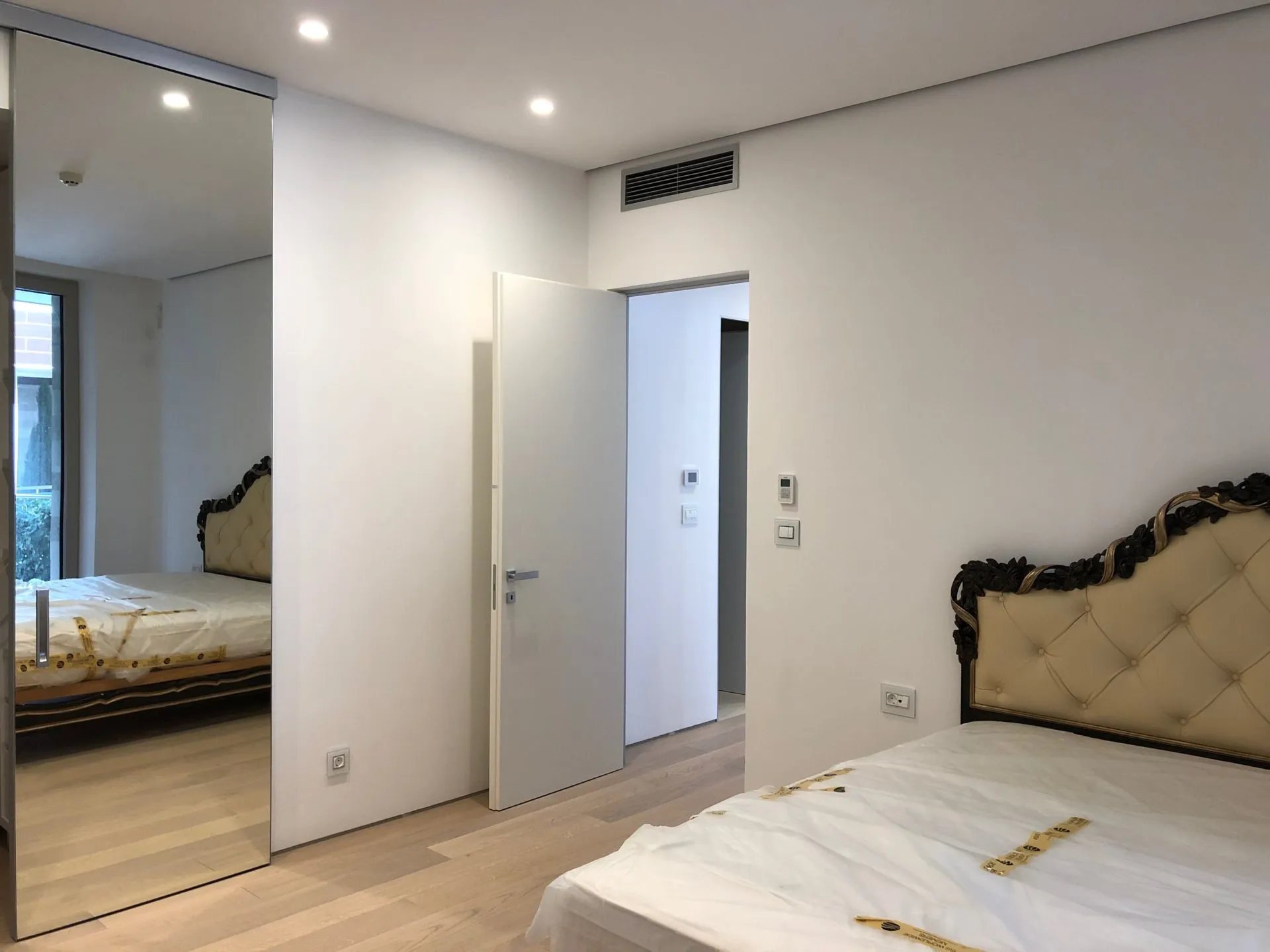 Modernes Schlafzimmer in einer Wohnung in Budva, Montenegro: Bett mit klassischem Kopfteil, Kleiderschrank mit Spiegeltüren und Parkett.