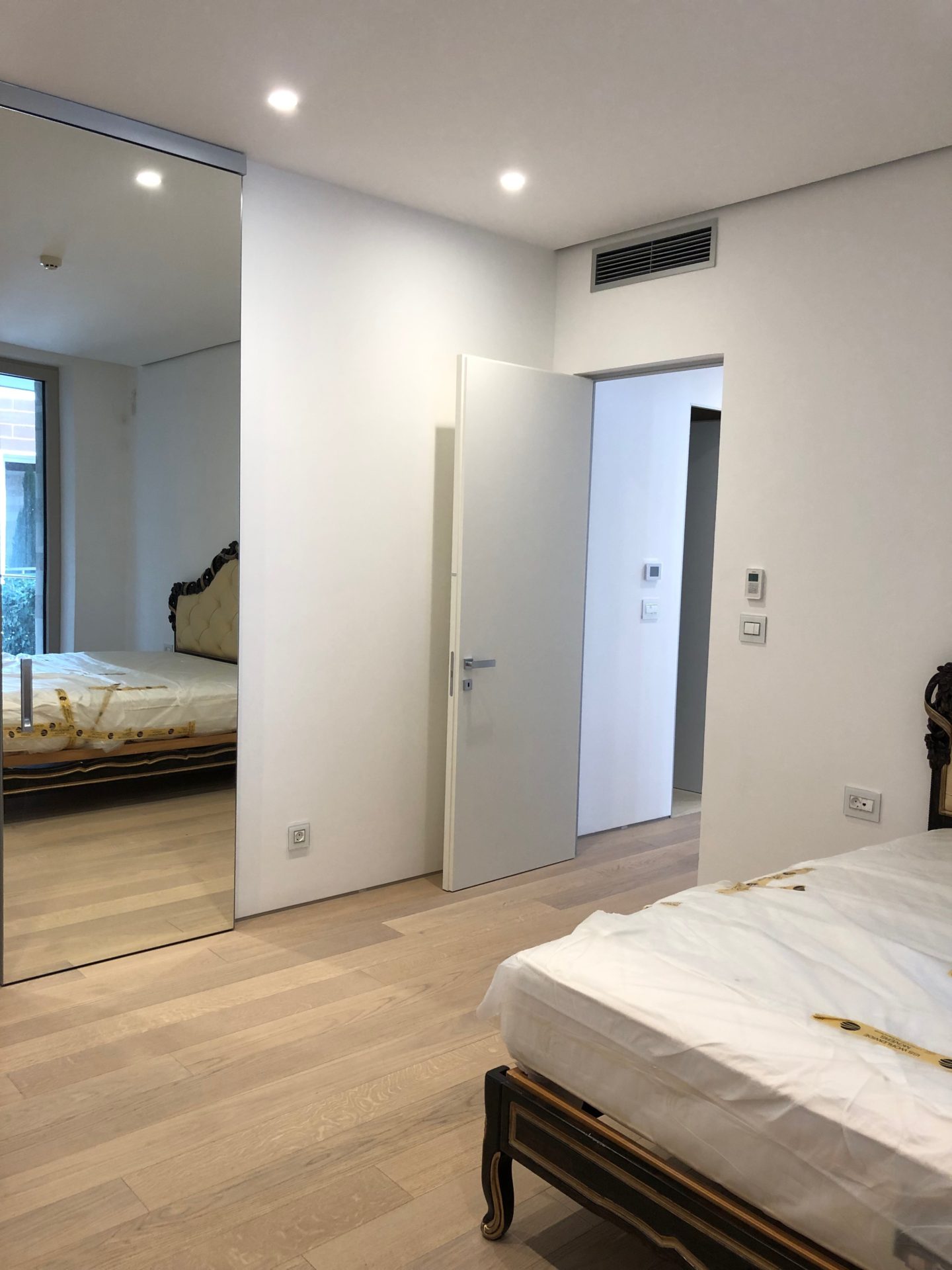 Modernes Schlafzimmer in einer Wohnung in Budva, Montenegro: Bett, Kleiderschrank mit Spiegeltüren, heller Parkettboden und integrierte Klimaanlage.