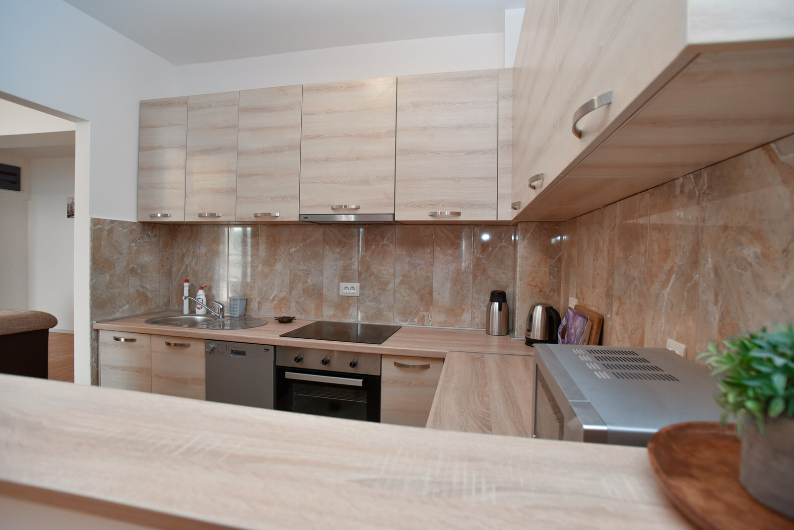 Moderne Küche mit hellen Möbeln und Marmoroptik-Rückwand in einer Wohnung zum Verkauf in Budva, Montenegro.