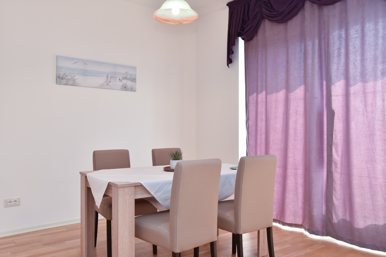 Essbereich im Wohnzimmer einer Wohnung in Budva, Montenegro: heller Tisch, Stühle und violette Vorhänge im Interieur.