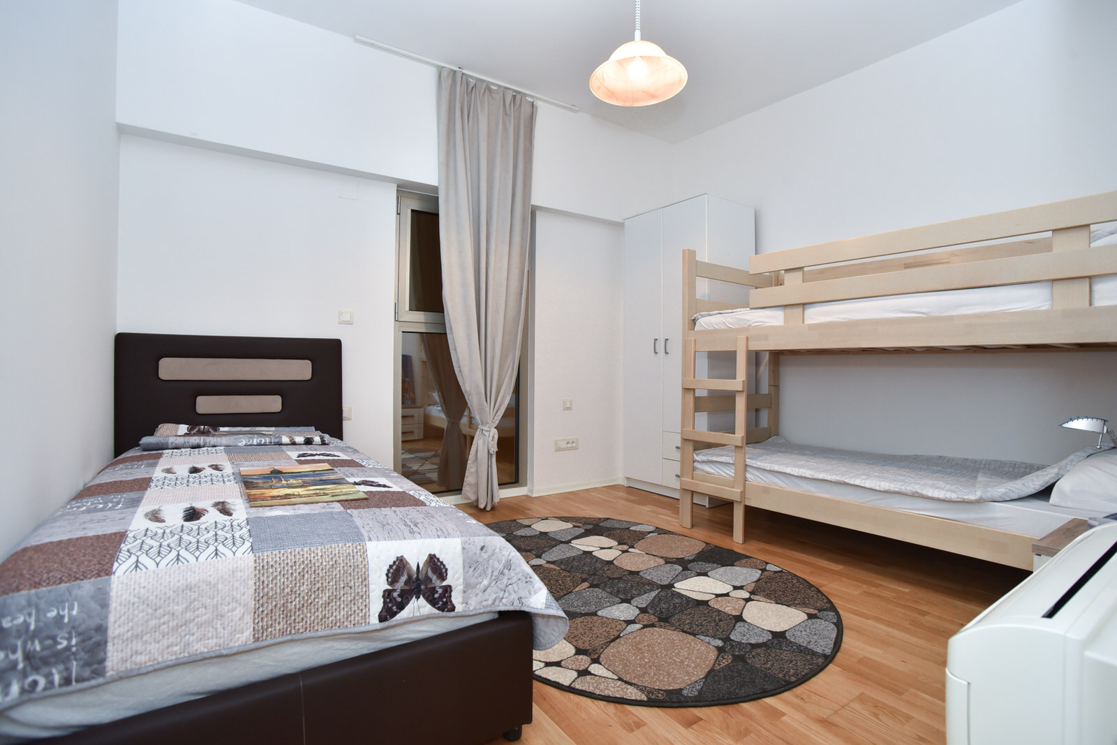 Helles Schlafzimmer in einer Wohnung in Budva, Montenegro: Doppelbett, Etagenbett, Kleiderschrank und Zugang zum Balkon.