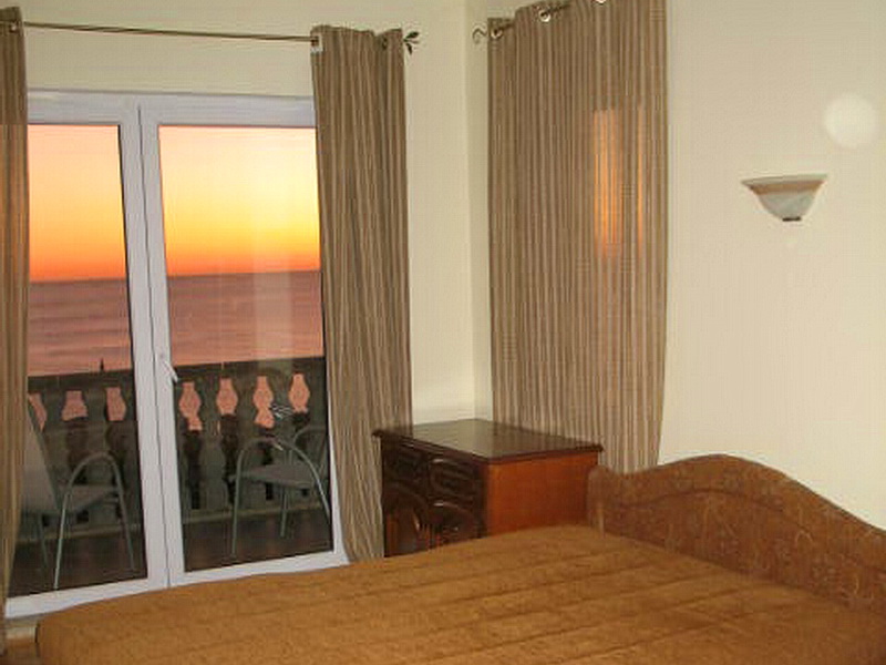 Bedroom with sea and sunset views in a house in Dobra Voda, Montenegro: double bed, dresser, and a furnished balcony.
