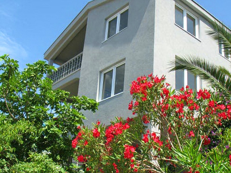 Three-story house in Dobri Vody, Montenegro, with balconies and a blooming garden in the foreground.